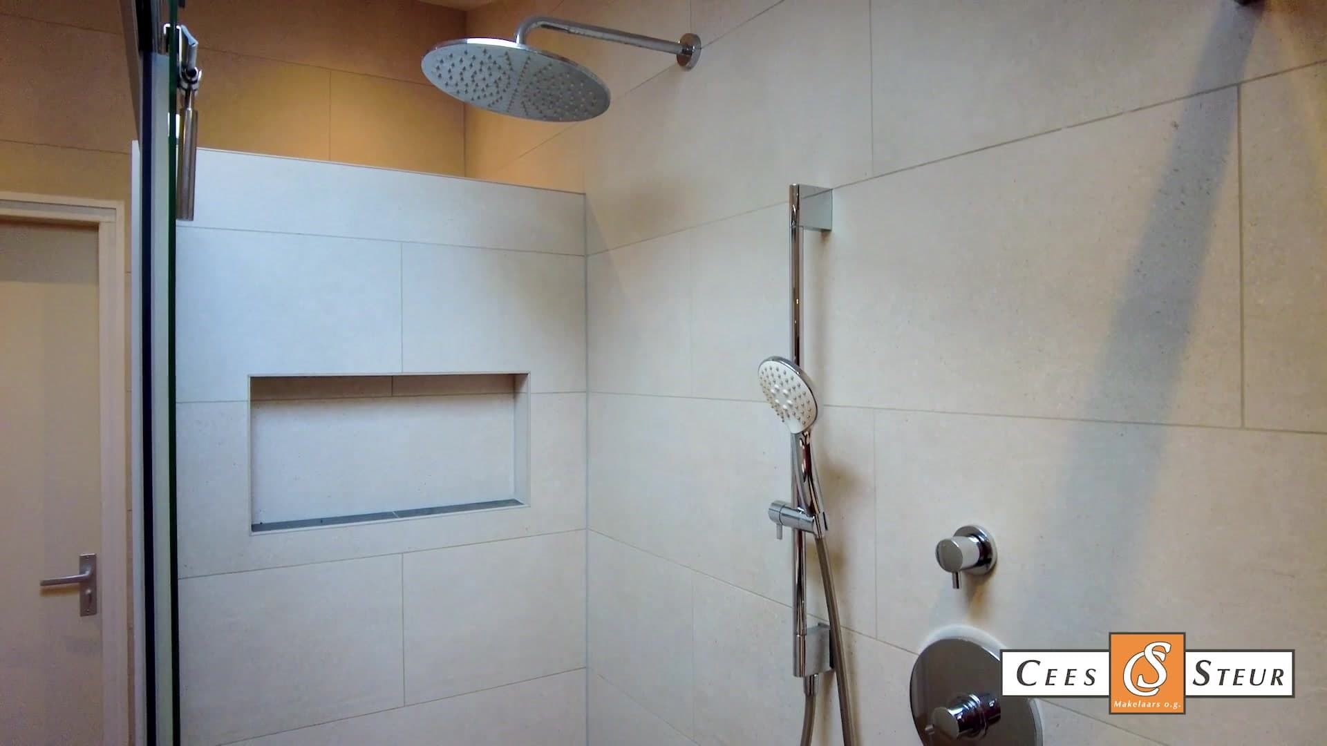 Still uit een woningvideo: een betegelde inloopdouche met regendouche en een nis, logo van het kantoor rechtsonder